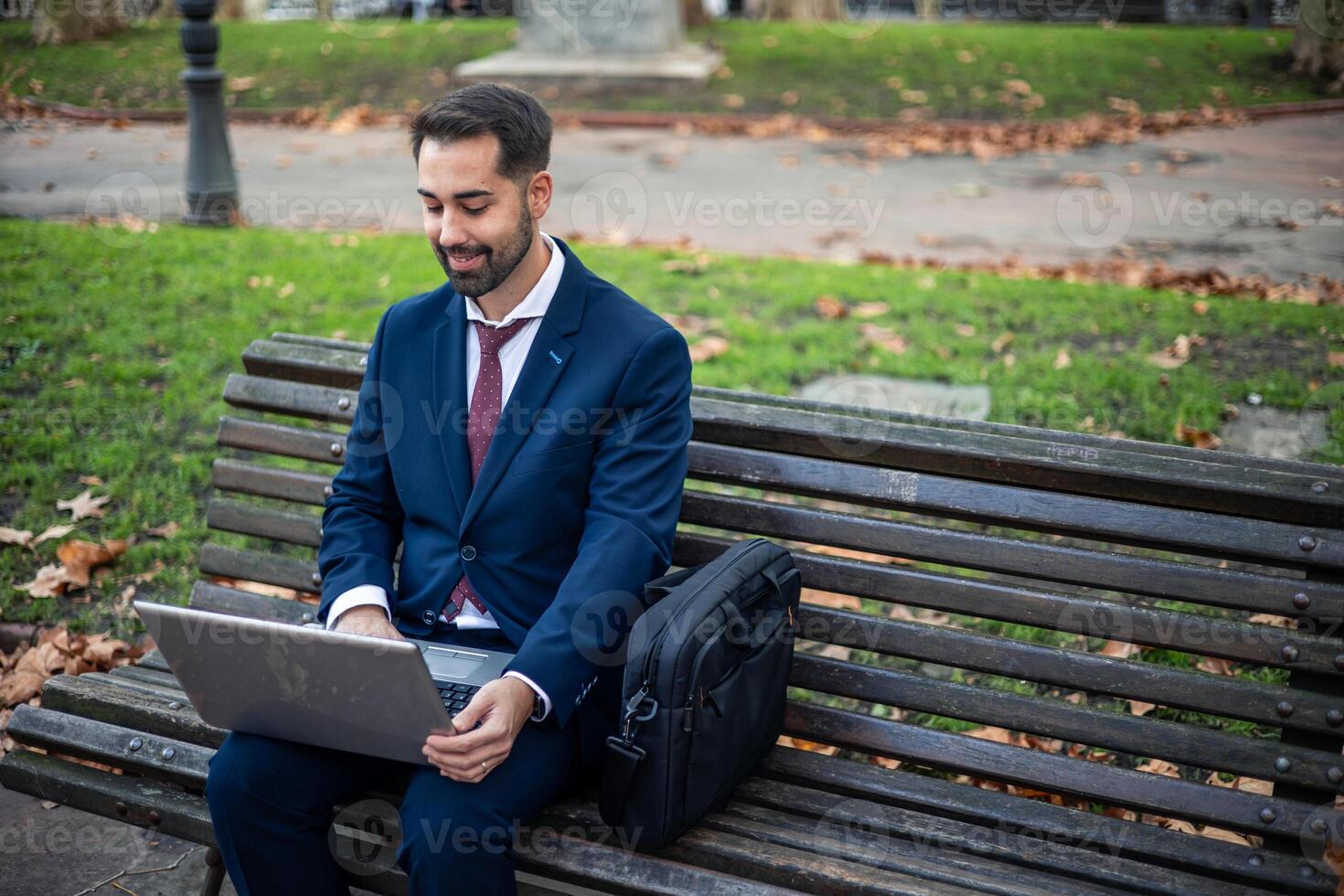 copyspace businessman sitting on a park bench working on his laptop photo