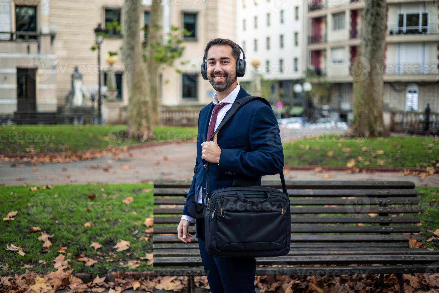 Smiling businessman wearing headphones walking in city park photo