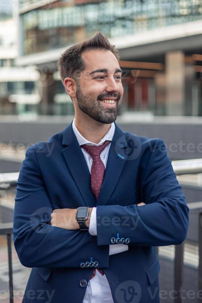 sonriente empresario vistiendo traje y reloj inteligente en pie con brazos cruzado en urbano ajuste foto