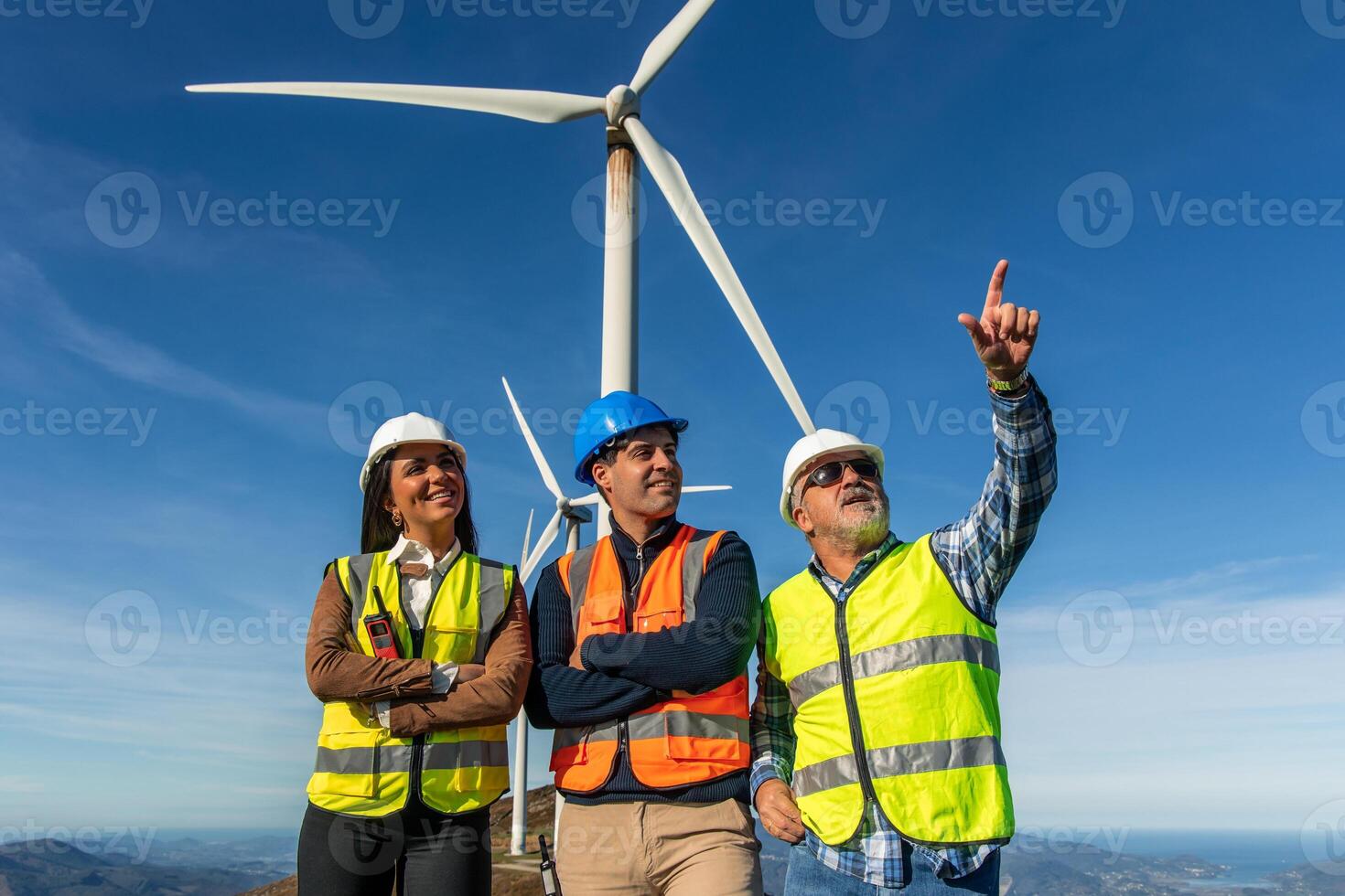 three multiethnic Engineers pointing at wind turbine in wind farm generating green energy photo