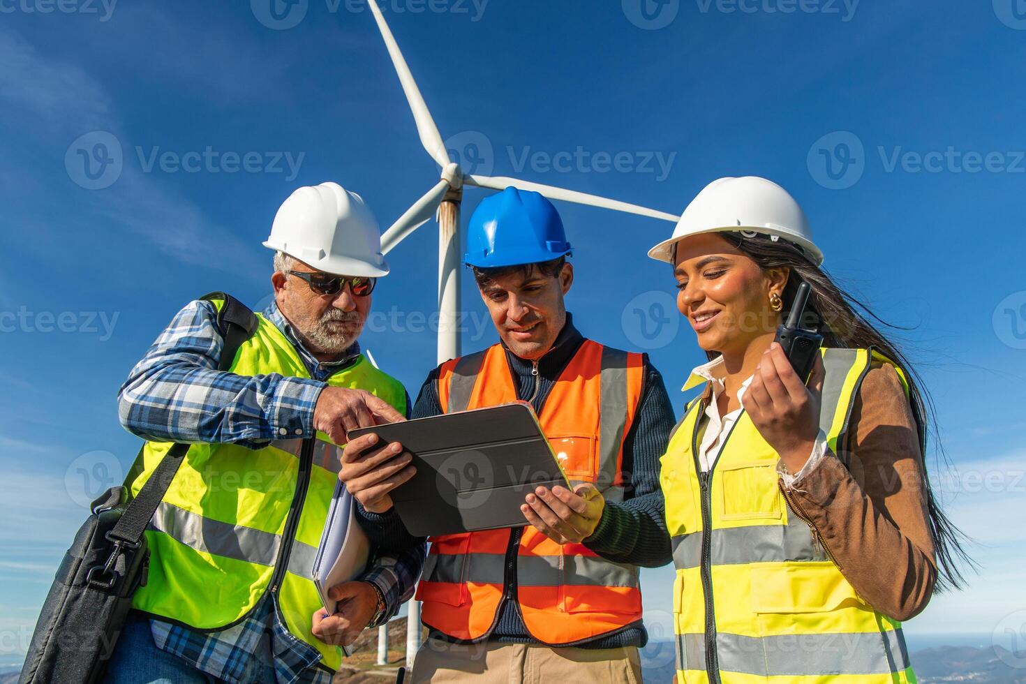 Three multiethnic Engineers using digital tablet, inspecting wind turbine for green energy photo