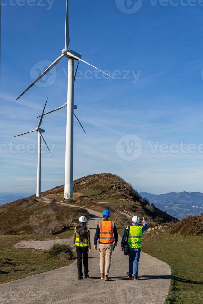 multiethnic Engineers walking and inspecting wind turbines on mountain top photo