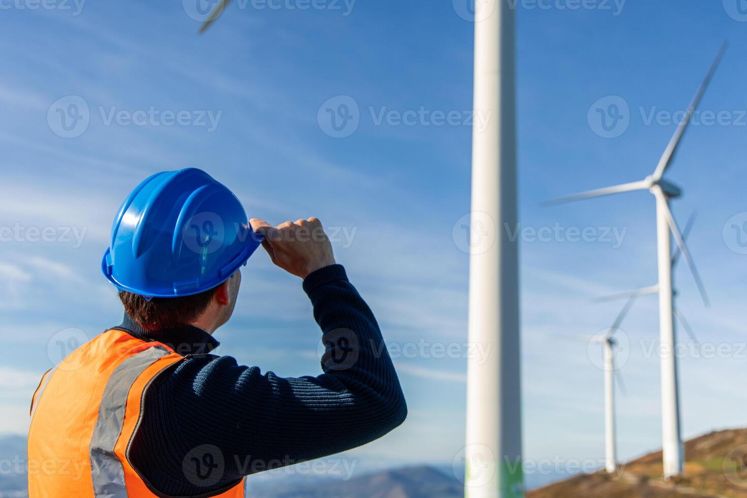 latin Engineer holding helmet and observing working wind turbines in mountainous area photo