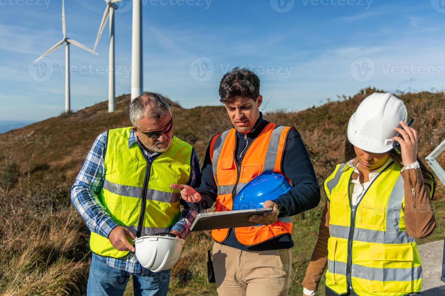 three multiethnic Engineers using tablet, discussing wind turbine maintenance project in field photo