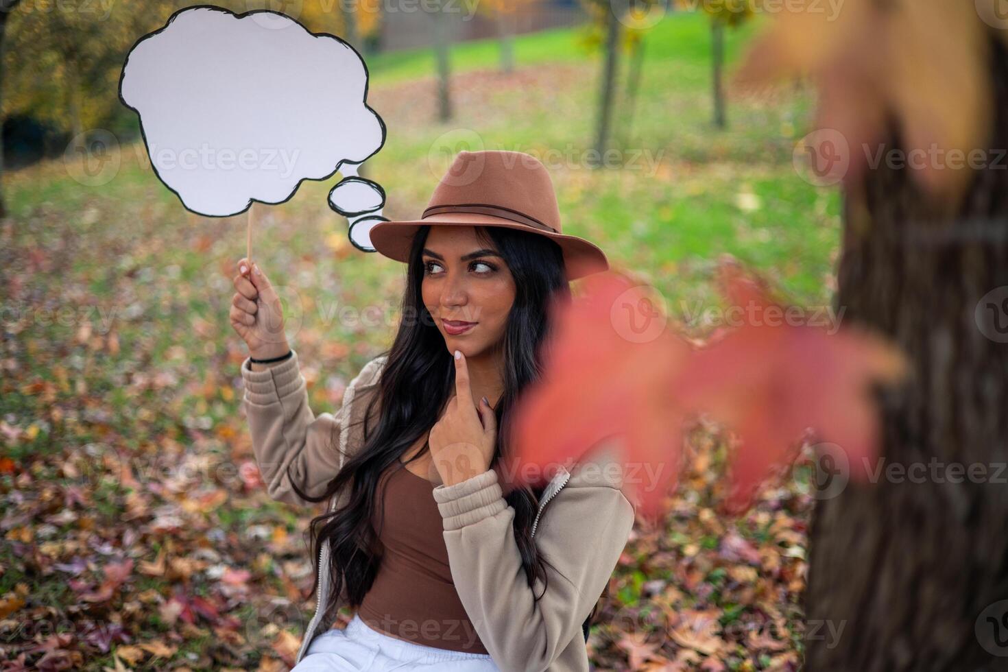 Pensive young latin woman holding empty thought bubble in autumn park photo