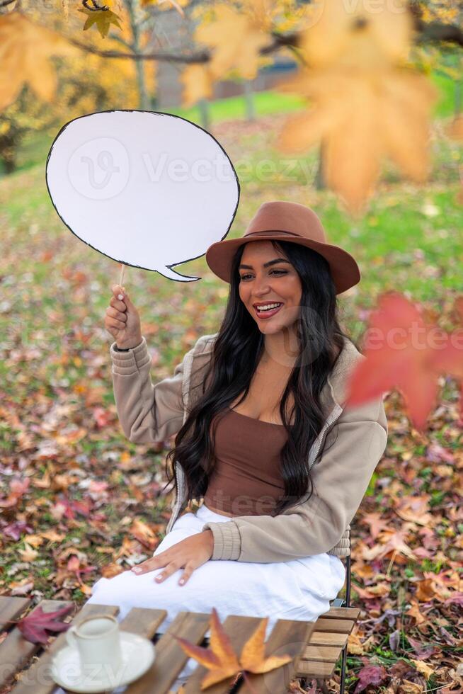 Young latin woman holding speech bubble in autumn park photo