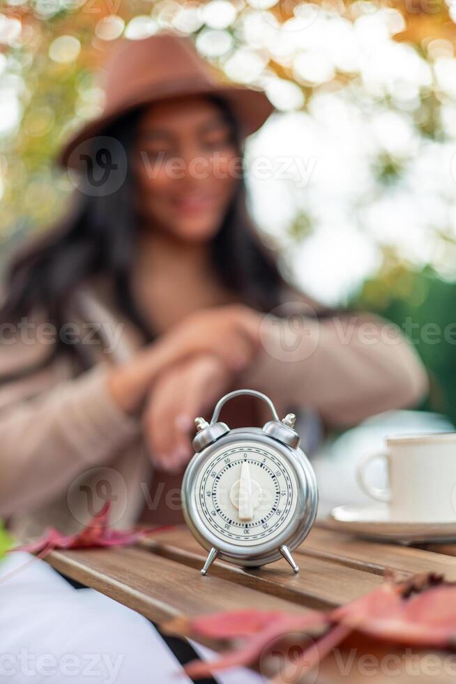Egg timer on a wooden table with blurred latin woman in autumn background photo