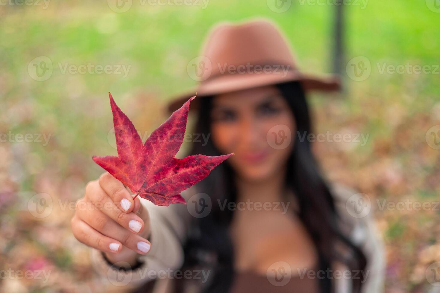 latin Woman showing red maple leaf during autumn in park photo