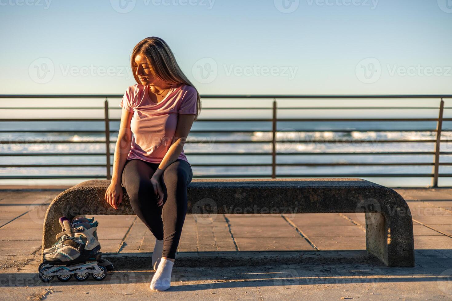 Young woman resting on bench after inline skating by the sea at sunset copyspace photo