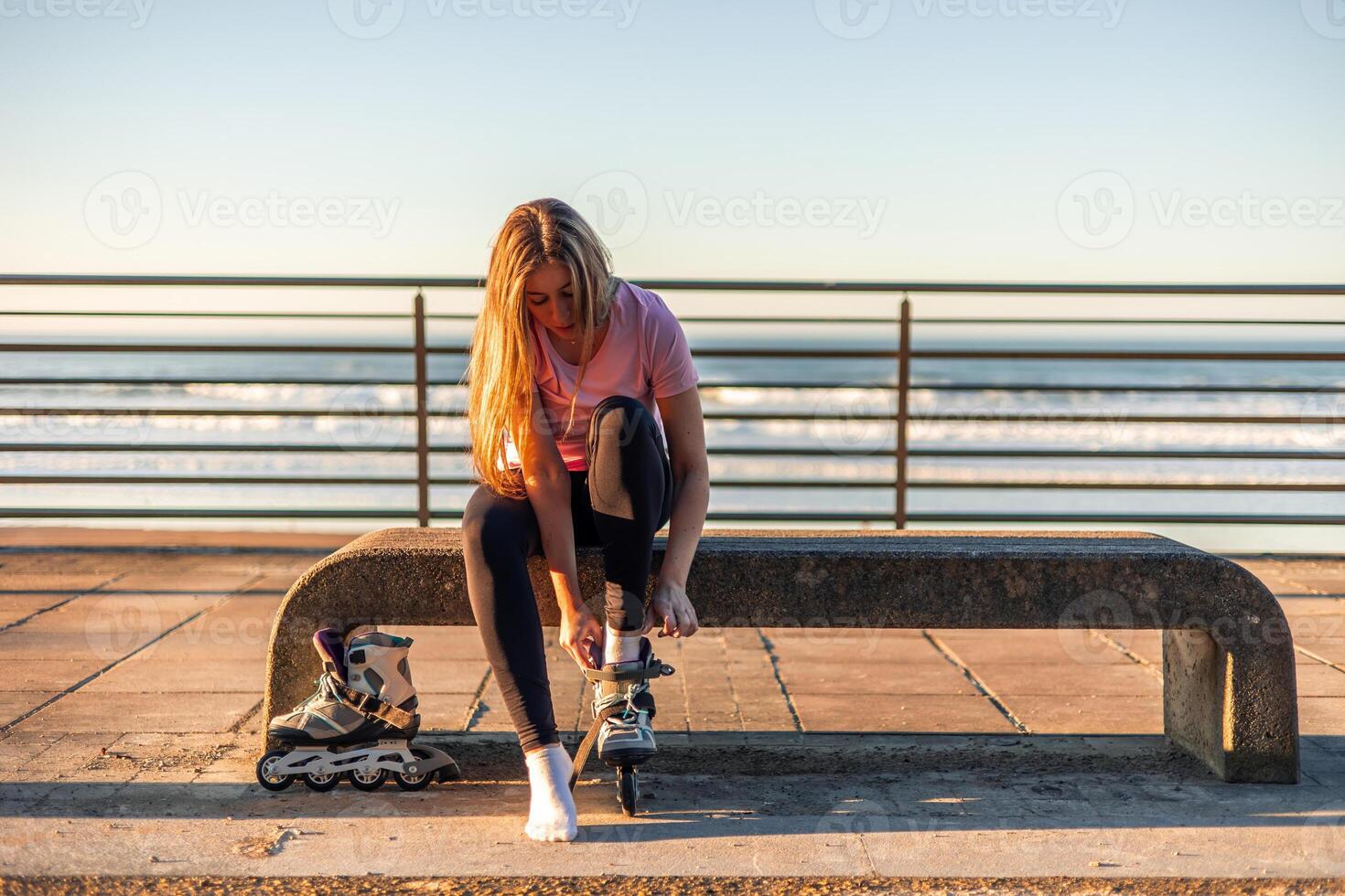 Young woman tying her inline skates sitting on a bench by the sea copyspace photo