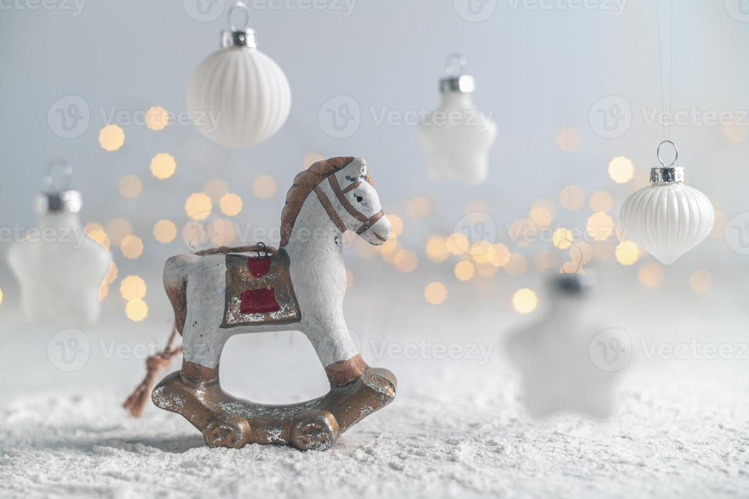 Charming christmas scene featuring a vintage rocking horse ornament on a snow-covered surface, surrounded by twinkling lights and hanging white star and ball ornaments photo
