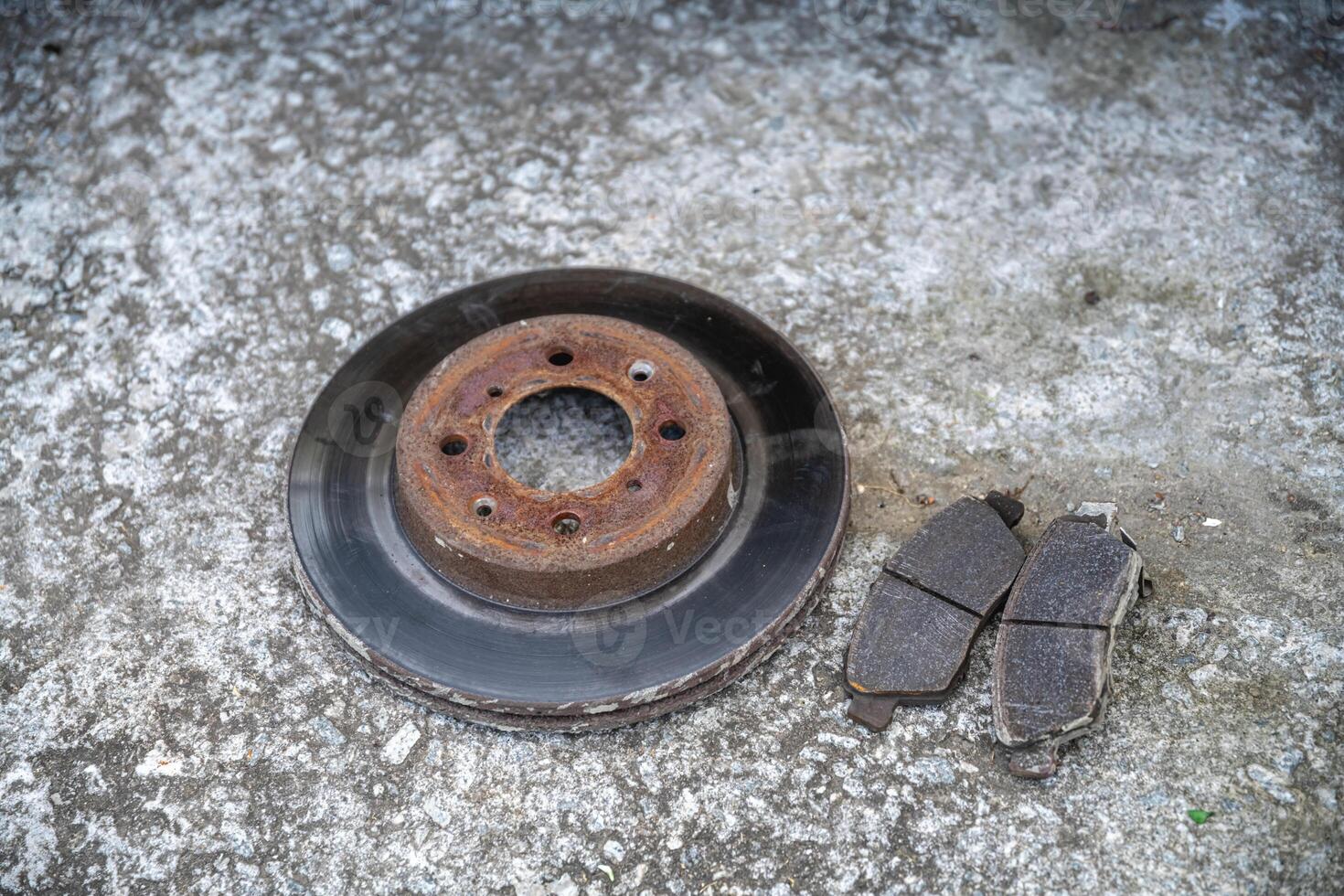 The old brake disc and brake pads are lying on a concrete surface, Repair of the car photo