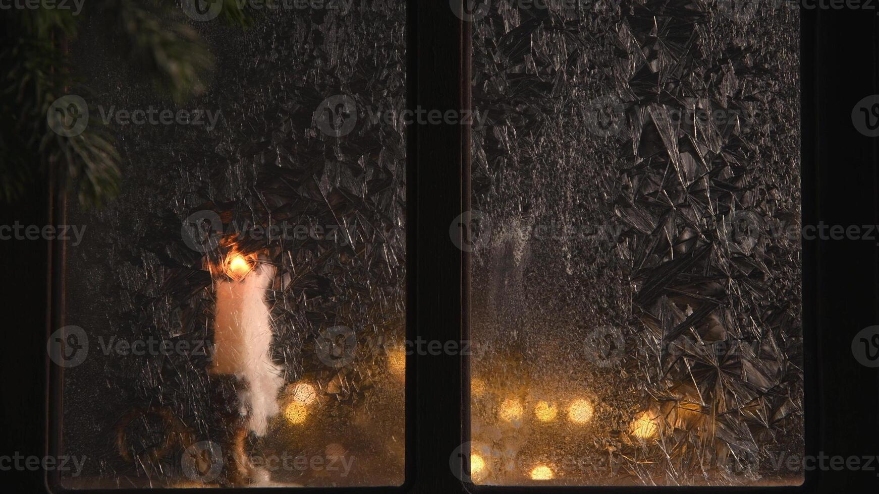 Burning candle and christmas lights create a warm glow behind a frosted window, evoking a cozy and festive atmosphere on a cold winter night photo