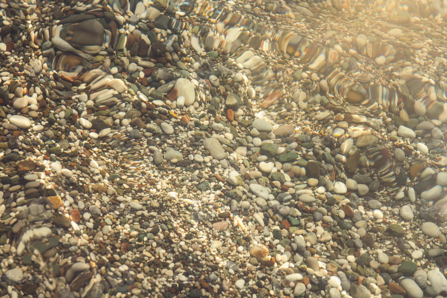 multi-colored stones under water on the sea, river. Natural background of stones, glare on the water photo