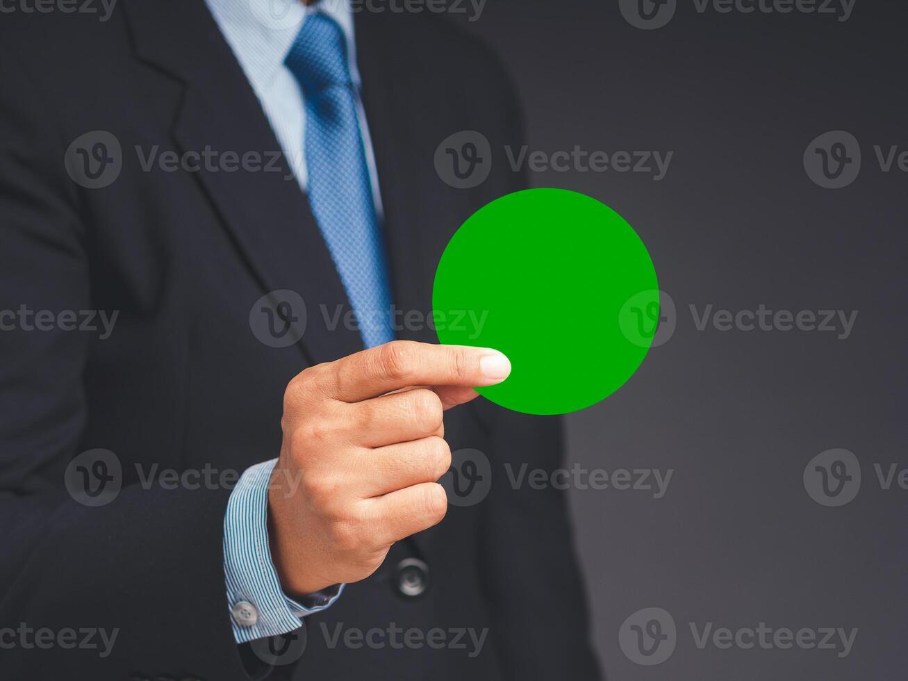 Close-up of hand businessman in a suit holding a blank green circle paper while standing on a gray background photo