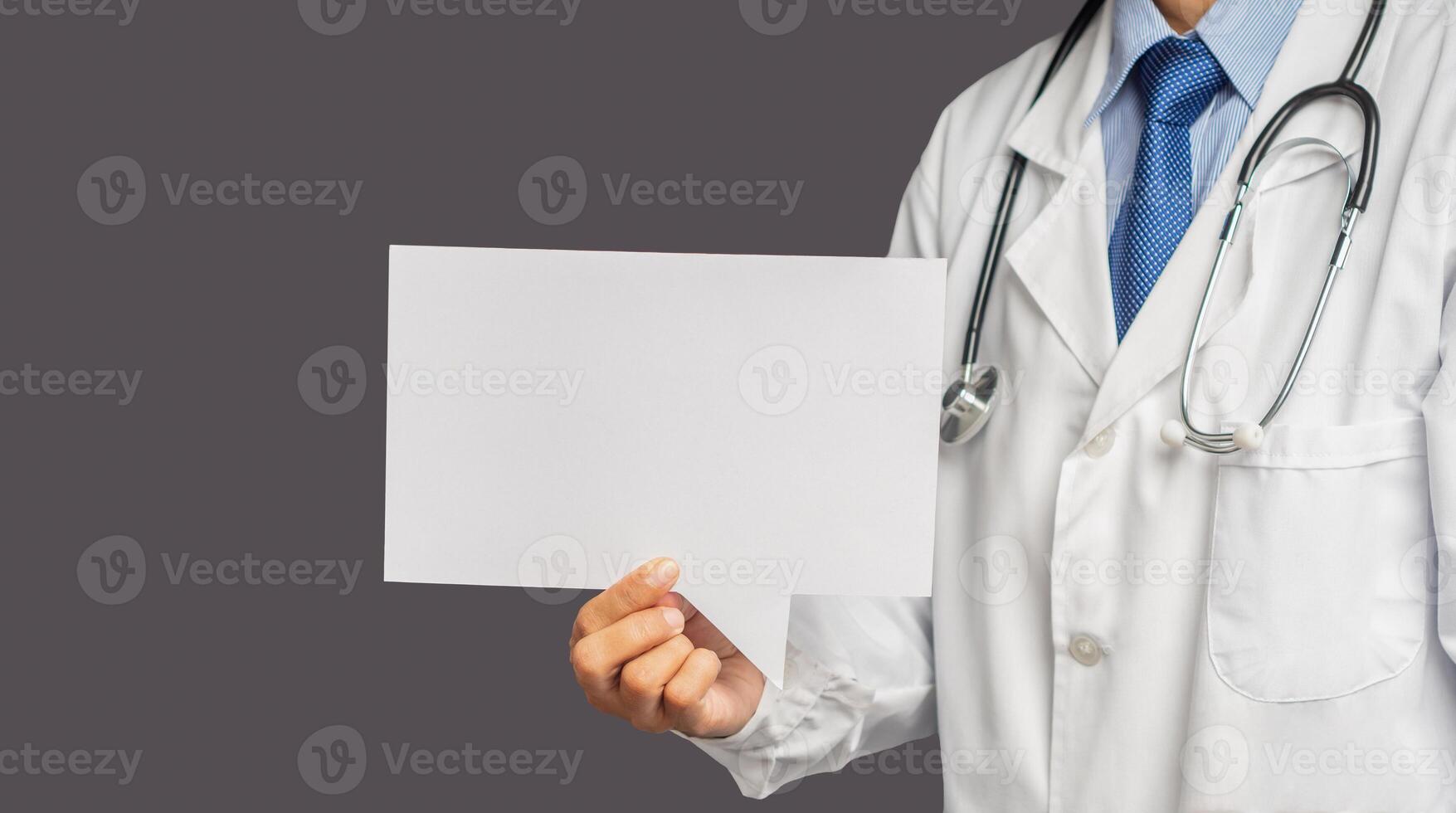 Doctor in uniform holding a white blank speech bubble while standing on a gray background photo