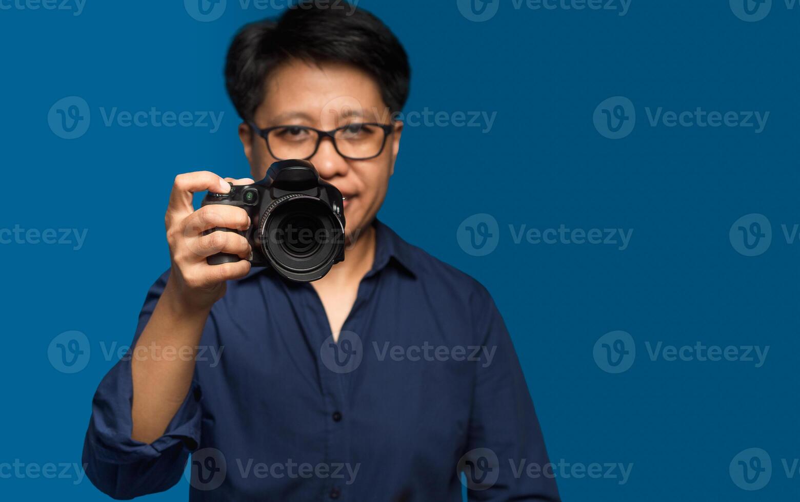 Portrait of a woman with short black hair holding a digital camera while standing on a blue background photo