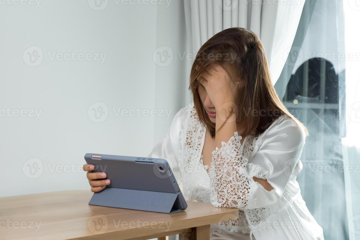 An Asian woman experiences eye strain and fatigue while reading her work schedule on a tablet at night. photo
