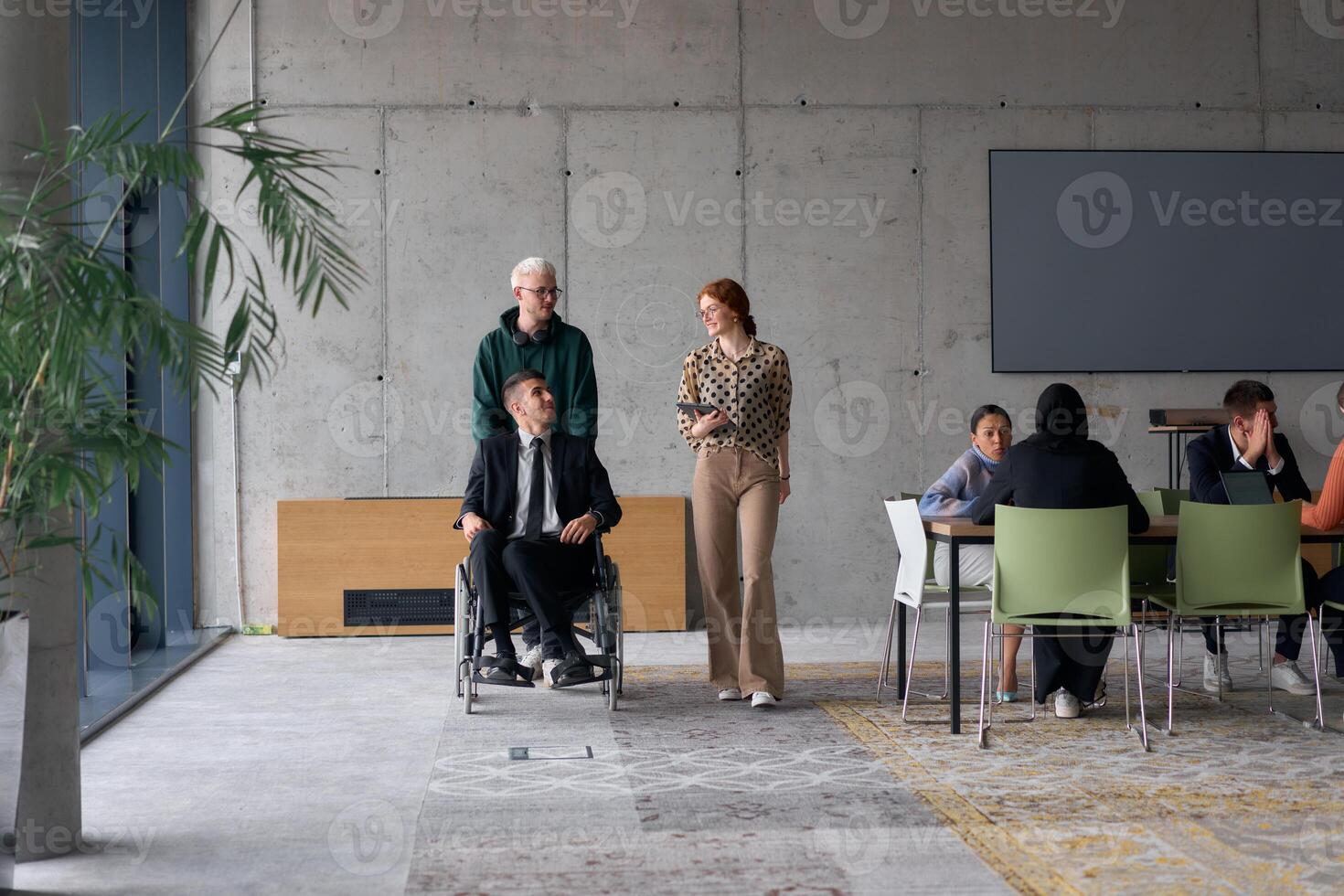 A diverse team of business colleagues, including a director in a wheelchair, engages in a collaborative discussion as they move together through a modern office space photo