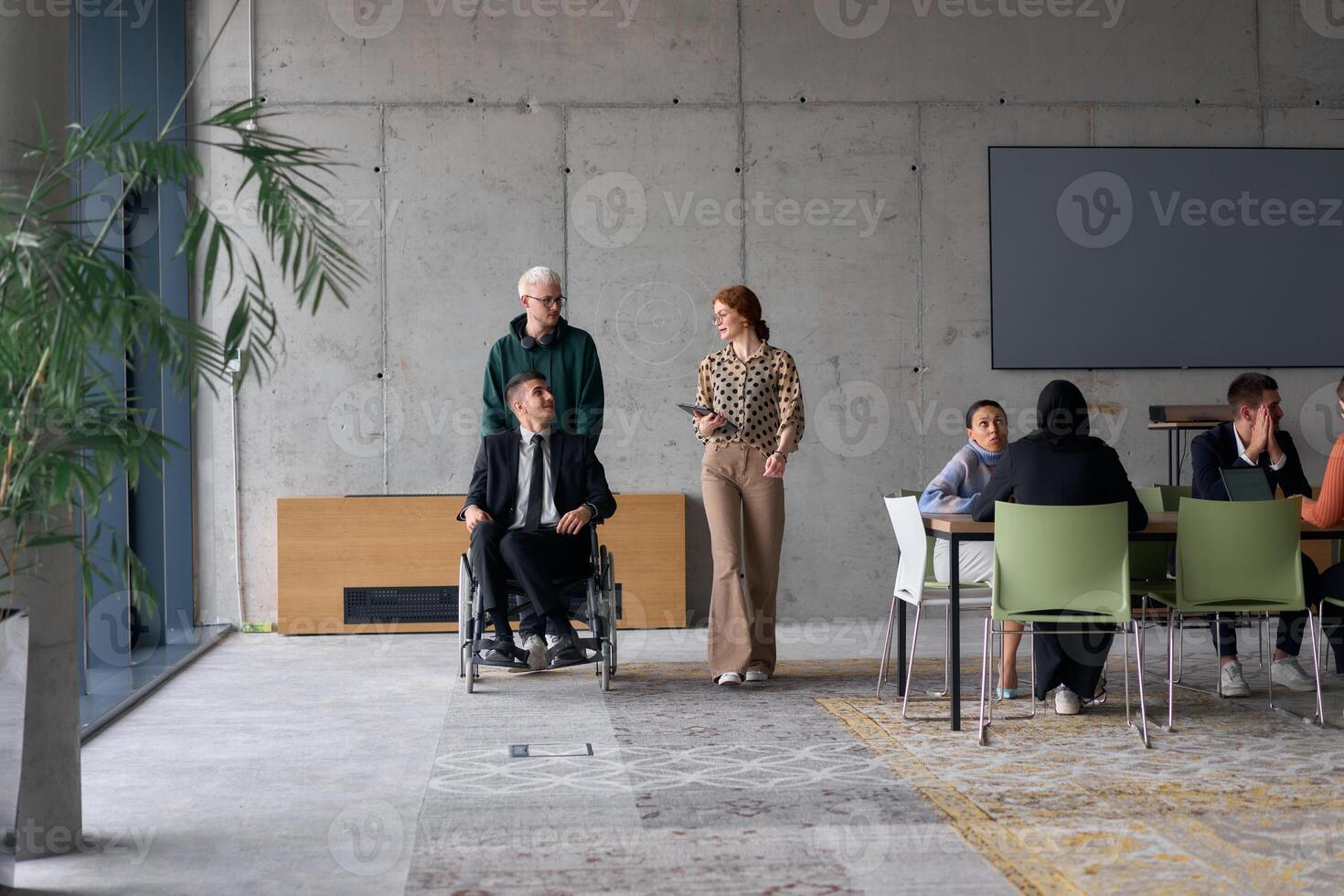 A diverse team of business colleagues, including a director in a wheelchair, engages in a collaborative discussion as they move together through a modern office space photo