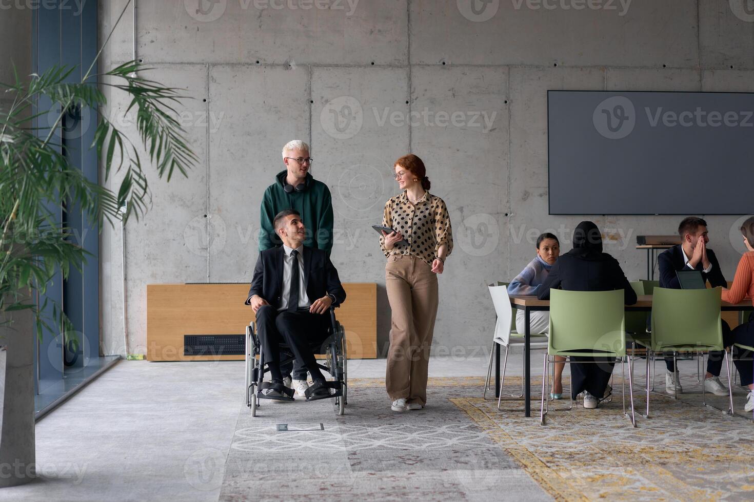 A diverse team of business colleagues, including a director in a wheelchair, engages in a collaborative discussion as they move together through a modern office space photo