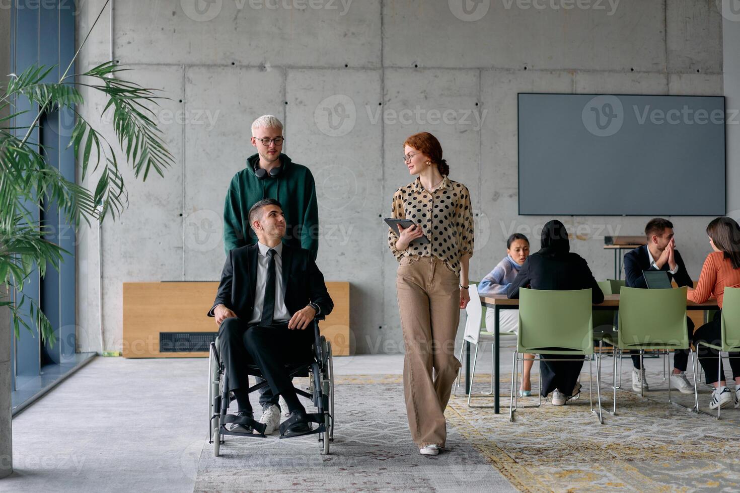 A diverse team of business colleagues, including a director in a wheelchair, engages in a collaborative discussion as they move together through a modern office space photo