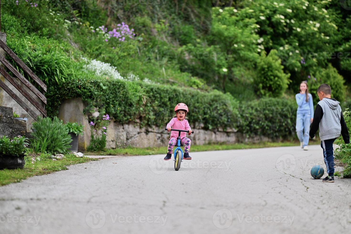 A group of children, including a boy and girl playing with a ball and their young friend riding a bike, enjoying a fun filled day in a natural outdoor setting photo