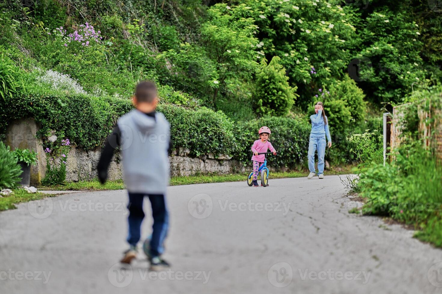A group of children, including a boy and girl playing with a ball and their young friend riding a bike, enjoying a fun filled day in a natural outdoor setting photo
