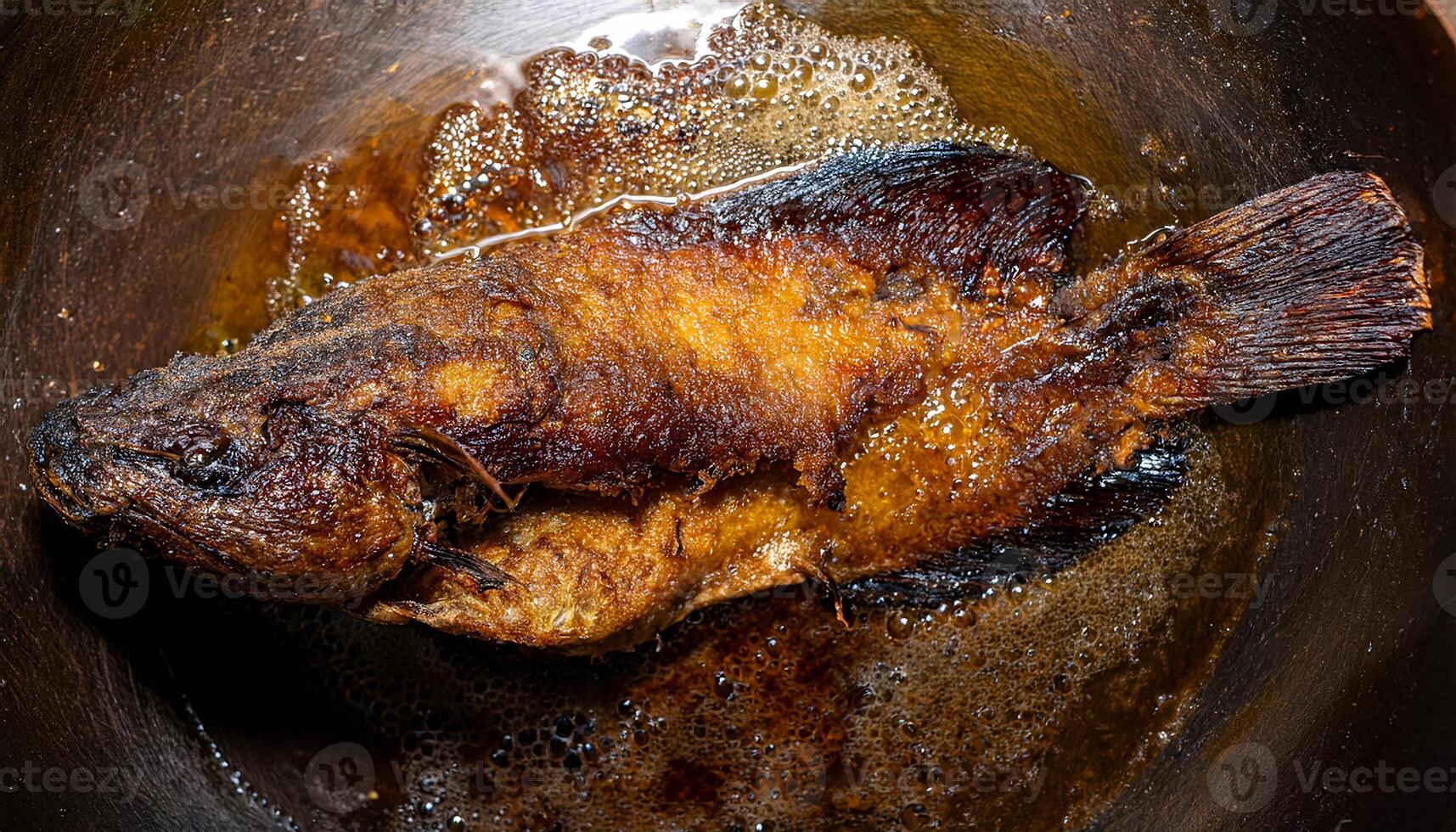 whole fried catfish in bubbling oil with crispy golden textures and deep-fried detail photo