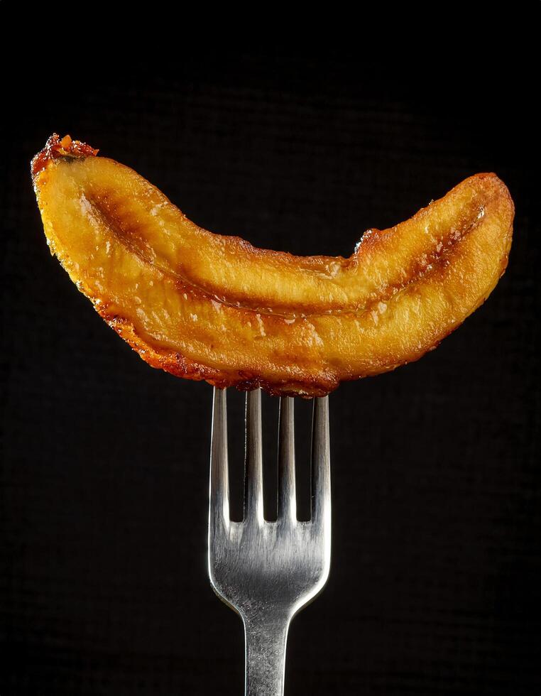 crispy fried banana slice with golden caramelized edges on a sleek fork showcasing tender sweetness and vibrant flavor against a dark background photo