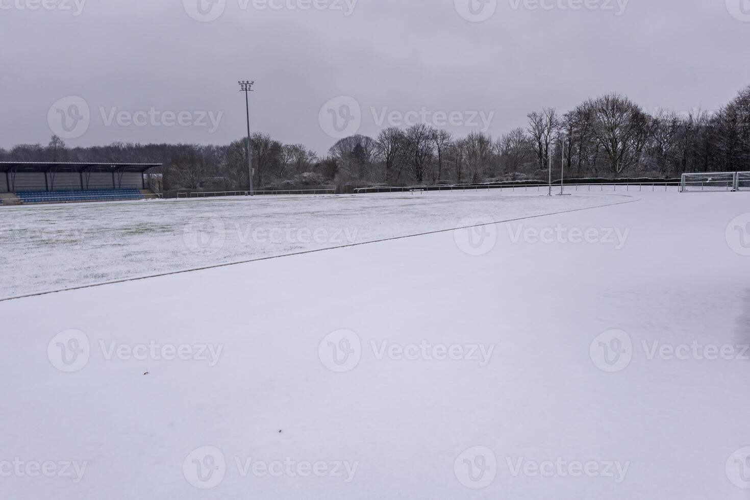 Snow covering soccer field during winter season with bleachers and cloudy sky photo