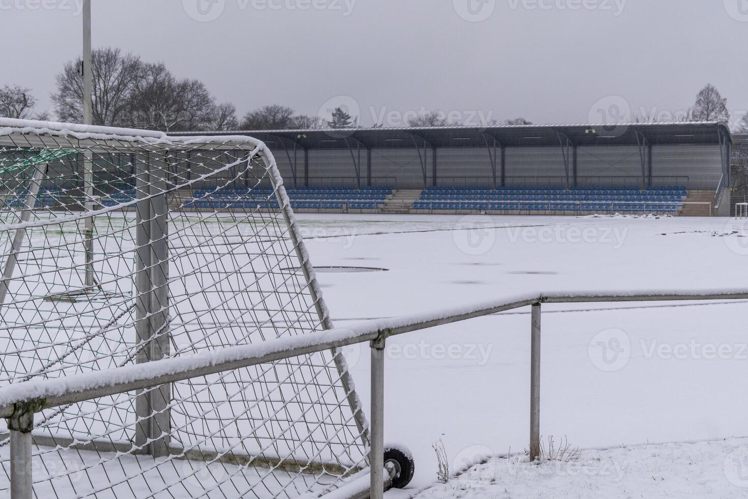 Snow covering soccer field and bleachers on overcast day photo