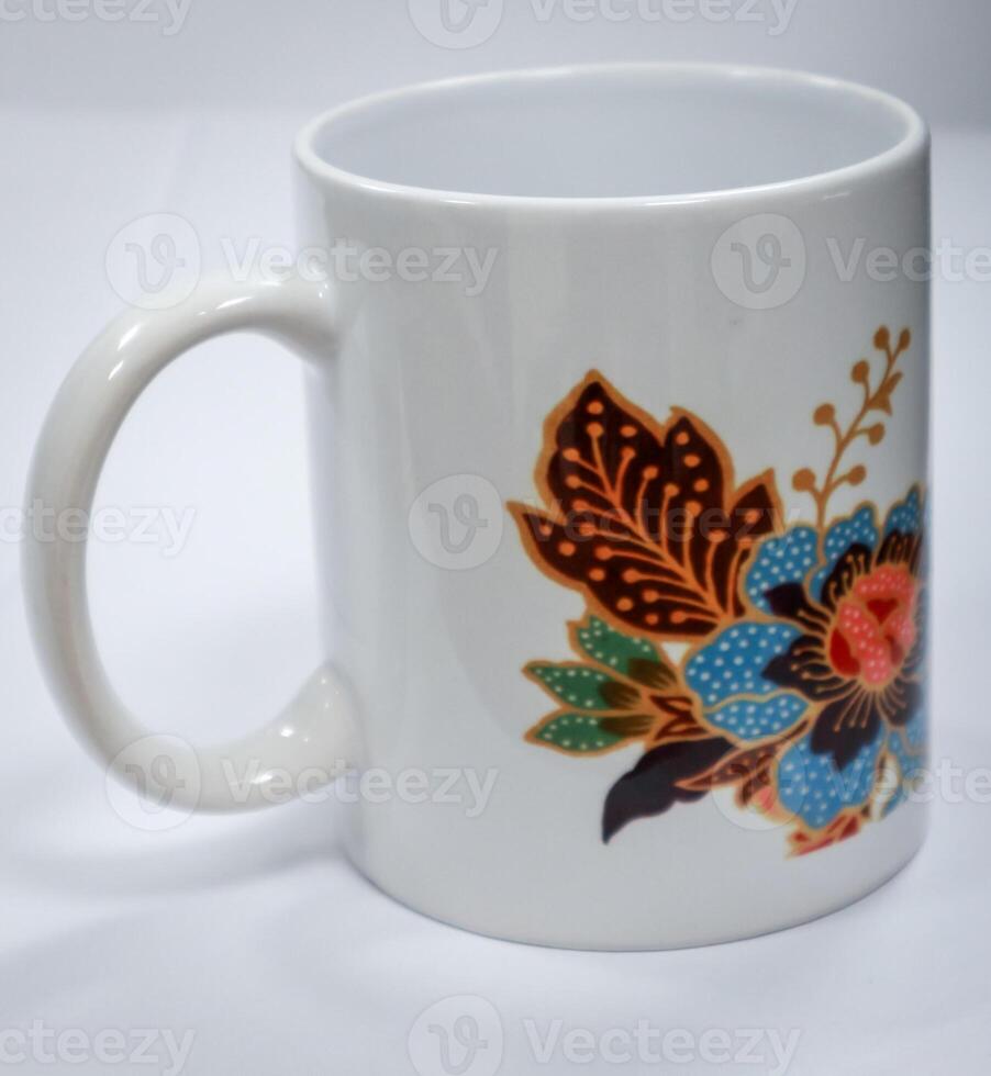 A white mug with a flower and leaf design using Indonesian batik motifs. The background is plain white with no people photo