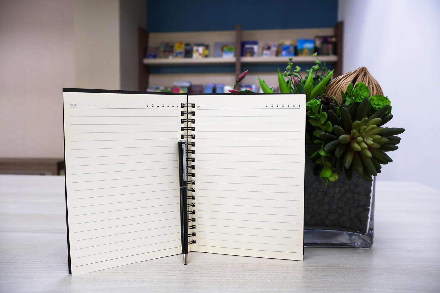 Notebook with lines page and black pen on wooden table background with artificial flowers as decoration. photo