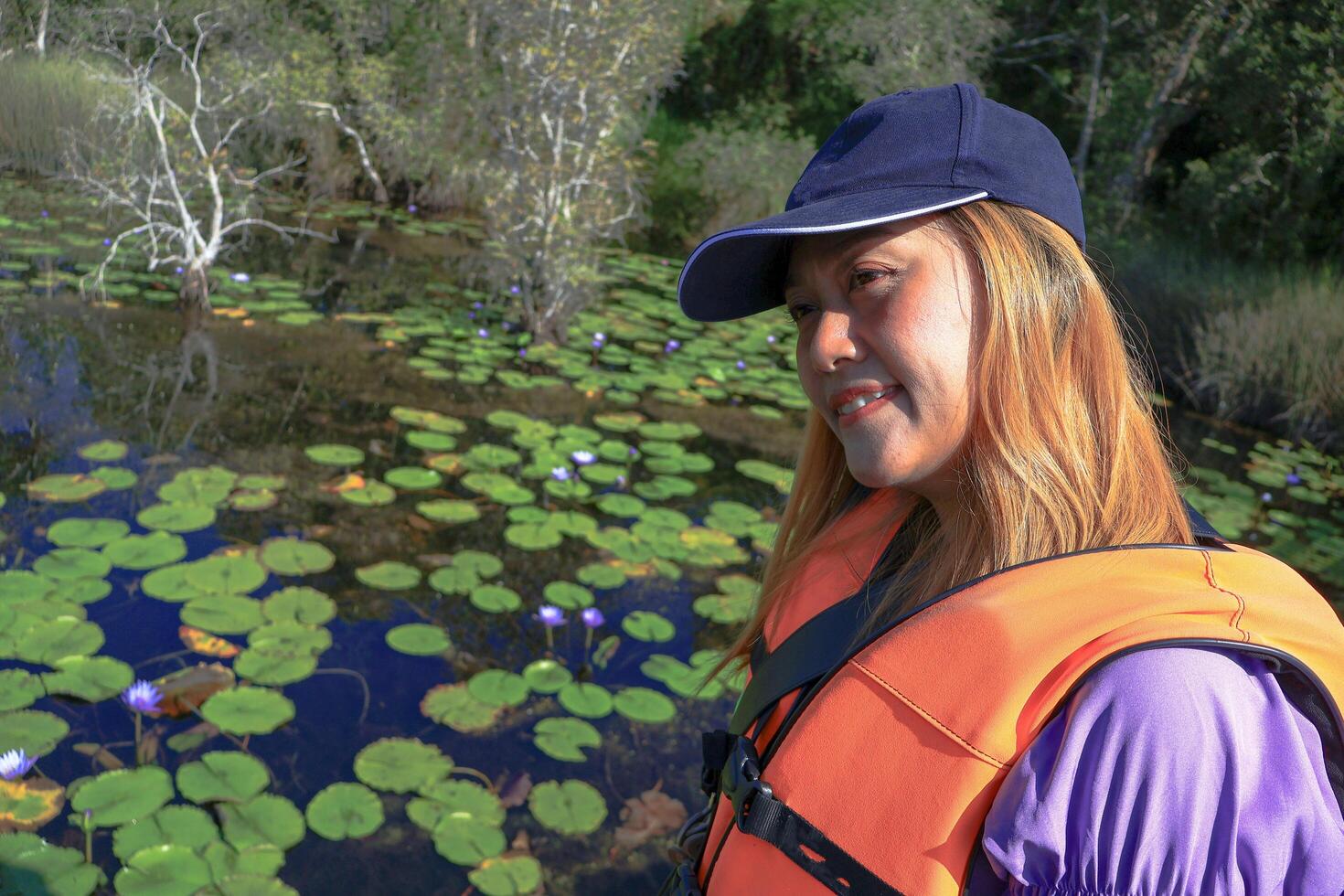 Asian women tourist stands smiling and takes a photo with a lotus pond in a botanical garden, a tourist attraction in Rayong Province, Thailand.