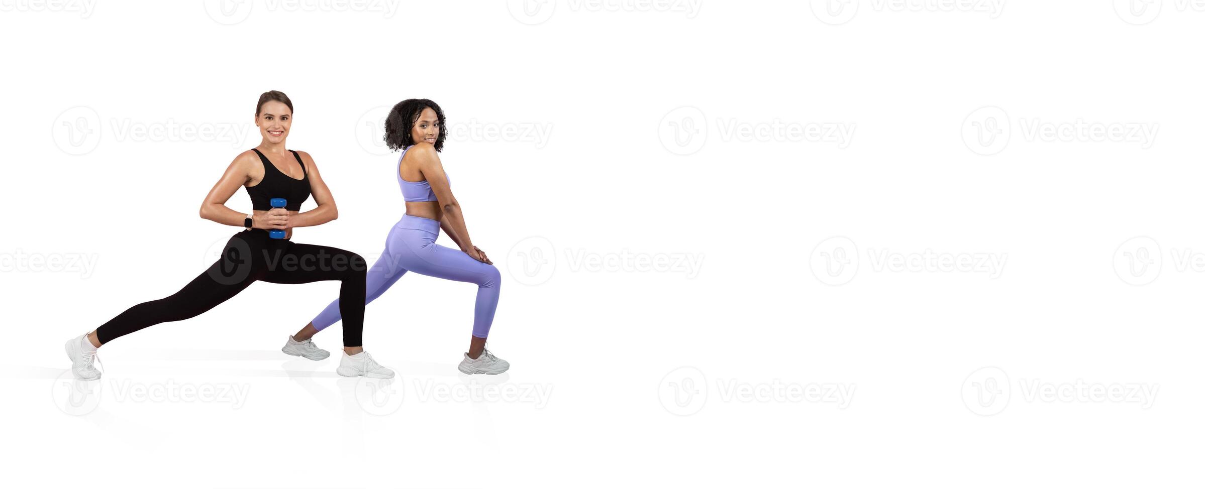 Two women are engaged in a lunge workout, demonstrating fitness techniques inside a well-lit studio. They are wearing colorful athletic apparel and focused on their exercises. photo