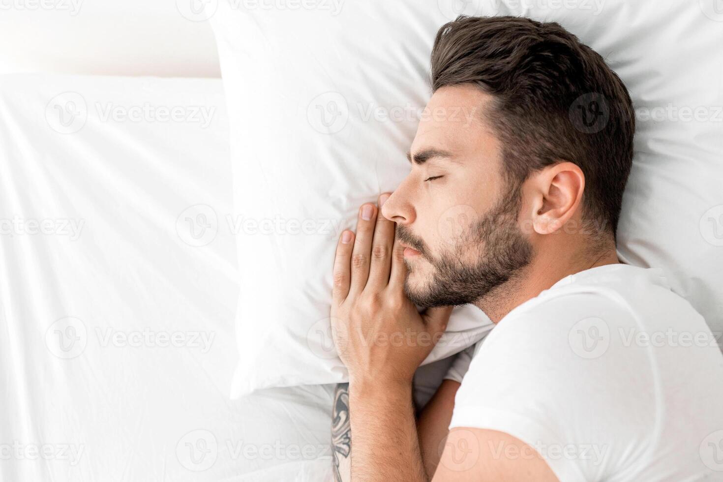 Asleep millennial man sleeping, resting peacefully in comfortable bed, lying with closed eyes, top view, free space. Recreation, deep male sleep, time to rest and nap concept photo