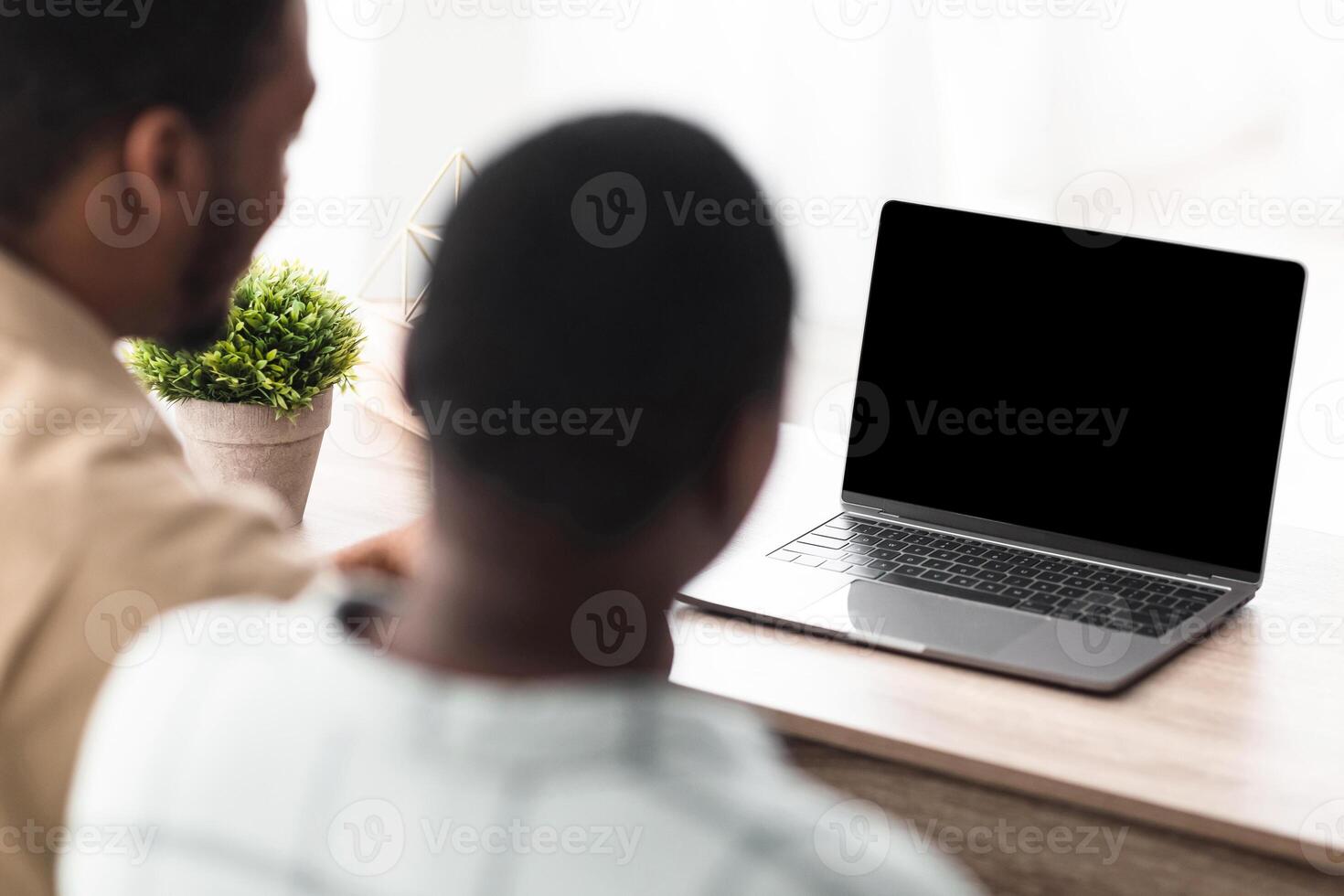 Rear View Of African American Couple Calling Using Laptop With Blank Screen Sitting At Desk Indoors. Modern Online Communication Concept. Selective Focus On Computer, Mockup photo