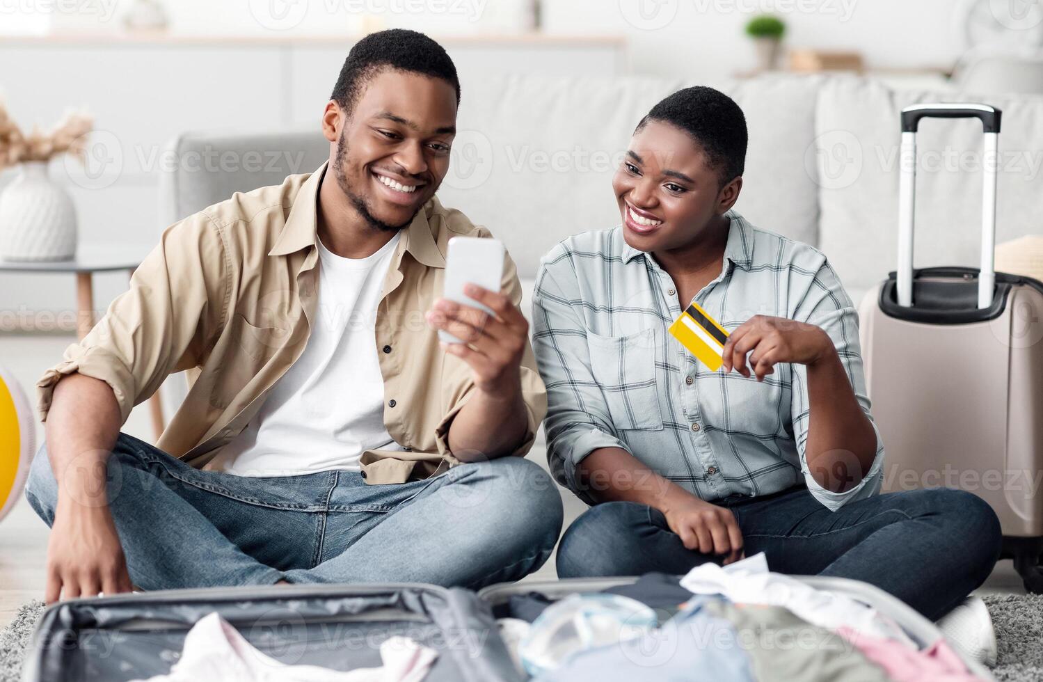 African American Travelers Couple Using Smartphone And Credit Card Booking Tickets Online In Travel Application Sitting Near Suitcase At Home. App For Tourists Concept. Selective Focus photo
