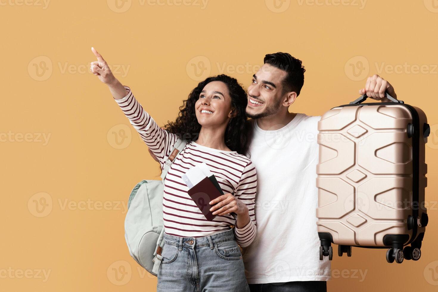Travel Advertisement. Joyful Arab Couple With Suitcase And Passports Pointing Away At Copy Space On Yellow Background, Happy Middle Eastern Travellers Demonstrating Free Place For Ad, Panorama photo