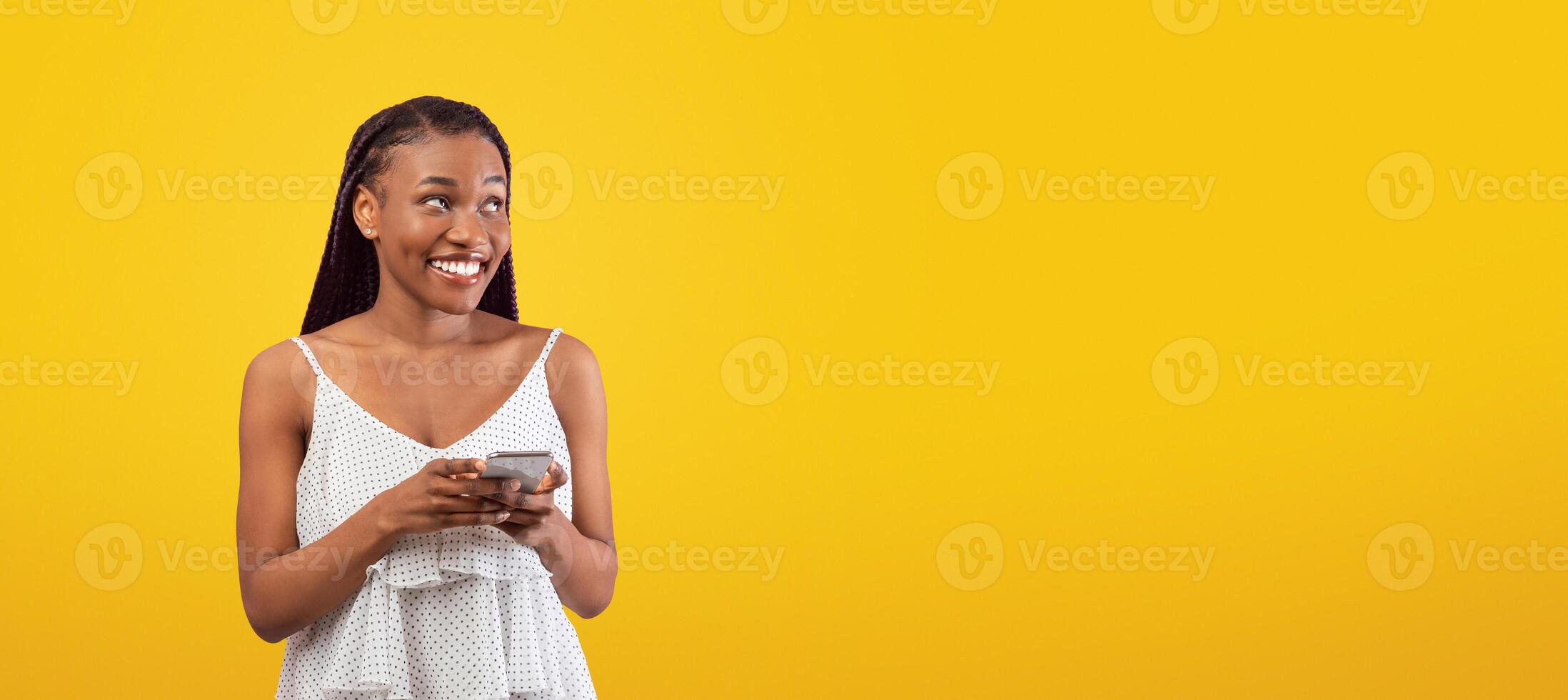 Cheery young black woman using smartphone, chatting online, watching , looking aside at empty space on pink background, banner design. African American lady surfing web, posting in social media photo
