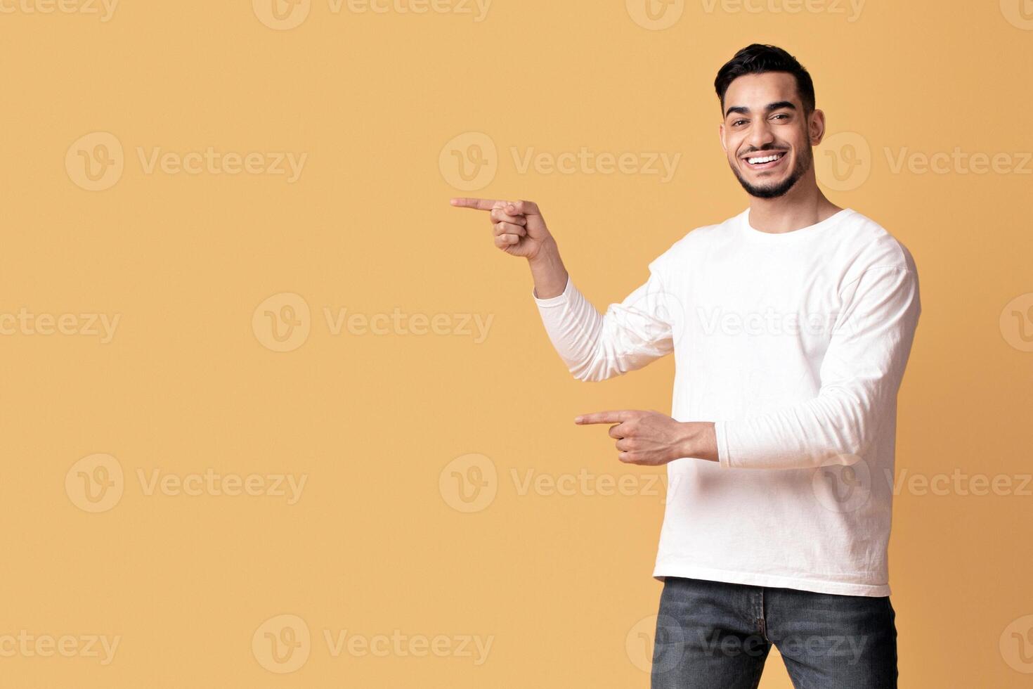 Check This. Happy arab couple pointing at copy space in the middle of yellow background, young middle eastern man and woman recommending something, showing free place for your design or advertisement photo