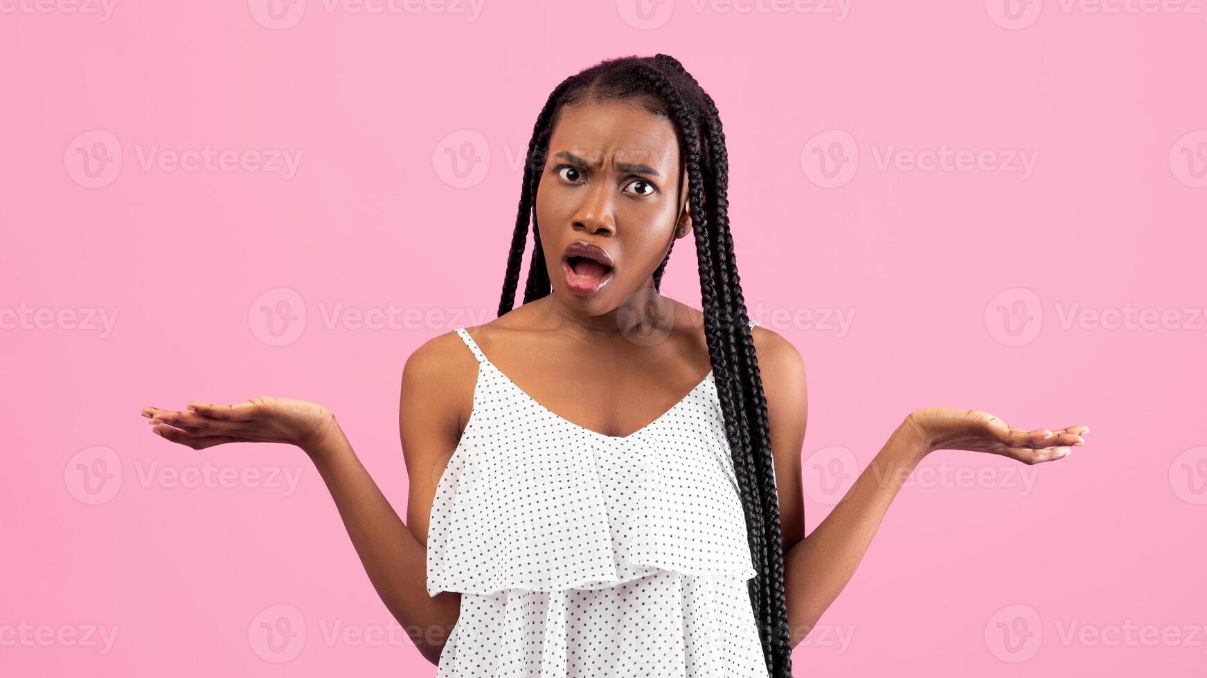 Irritated African American woman showing I DON'T KNOW gesture, shrugging shoulders on pink studio background. Annoyed black lady cannot understand something, gesturing WTF photo