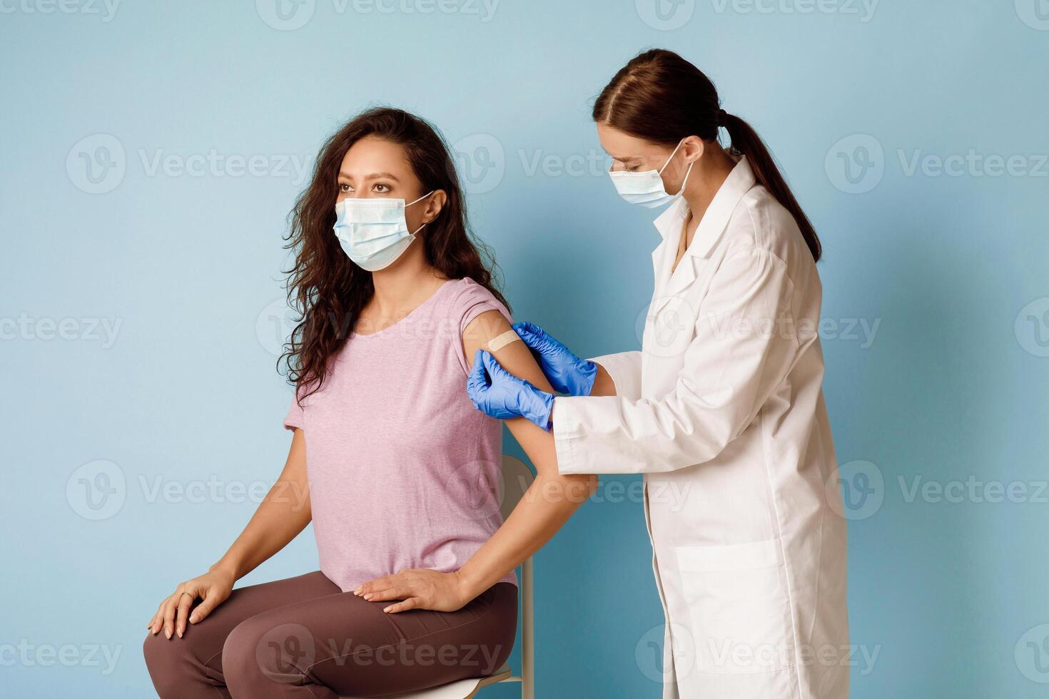 Covid-19 Vaccination. Female Patient Getting Vaccinated, Nurse Applying Plaster On Arm After Injecting Coronavirus Vaccine On Blue Studio Background. Covid Immunization Campaign Concept photo