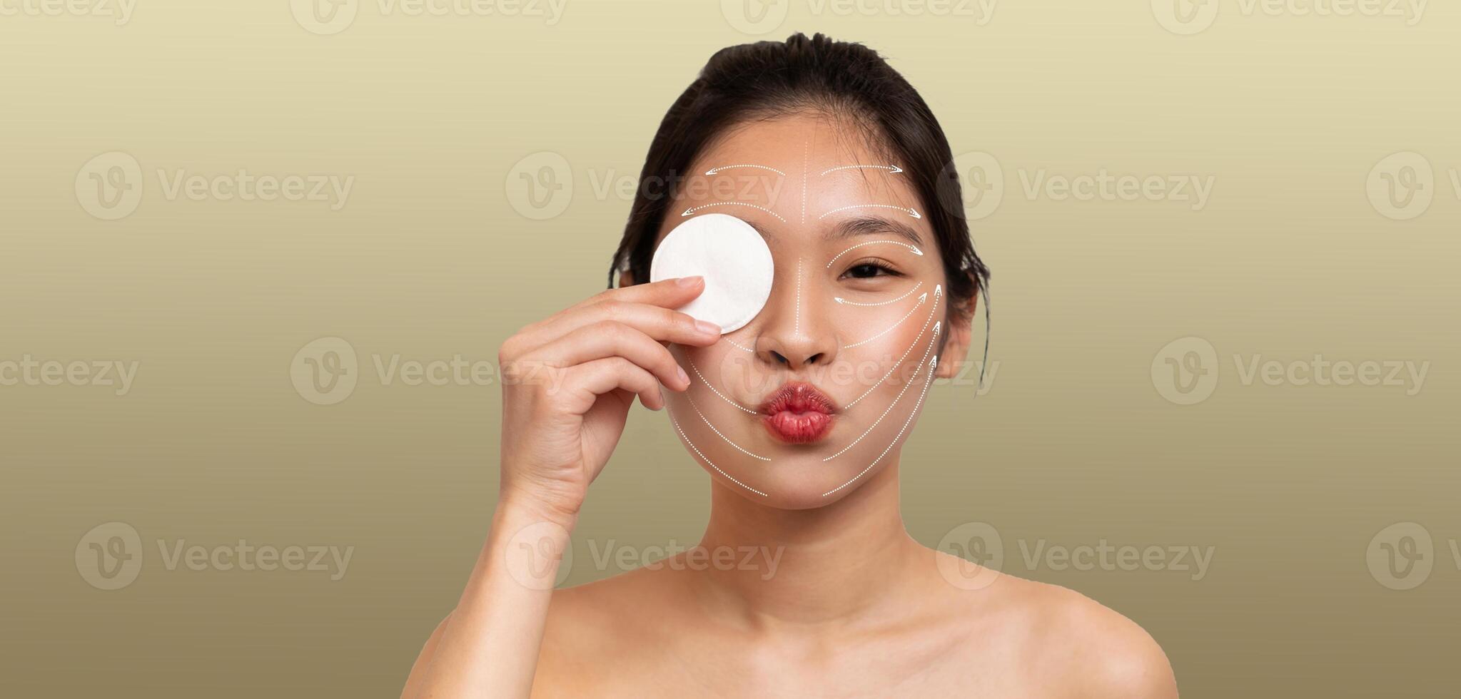 Asian lady is pampering herself during a skincare routine by holding a cotton pad to her face. She appears relaxed and focused, showcasing a moment of beauty care and self-care. photo