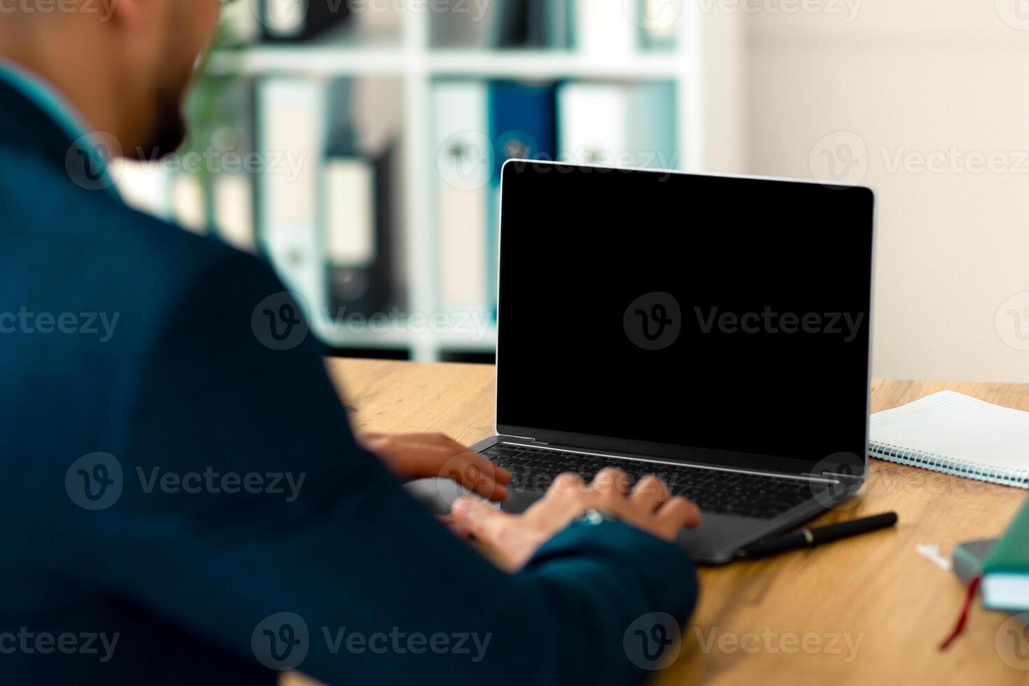 Unrecognizable Arab entrepreneur working on laptop pc with blank screen at office, mockup for website design. Company employee using portable computer with space for ad indoors photo