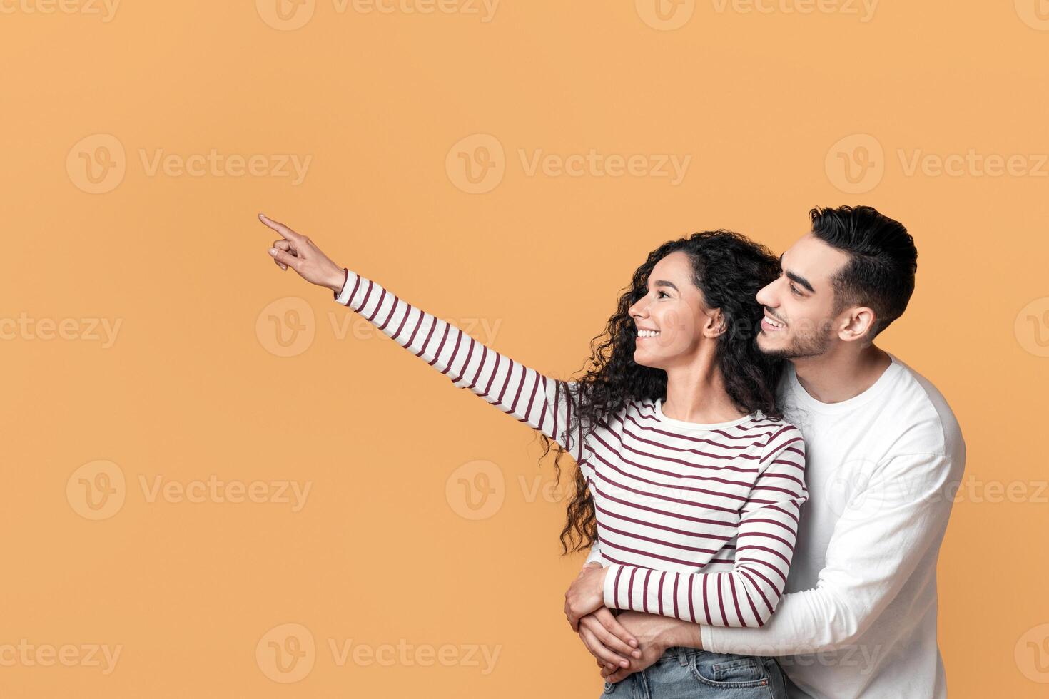 Family Offer. Happy Millennial Arab Spouses Embracing And Pointing Aside At Copy Space, Smiling Middle Eastern Couple Demonstrating Free Place For Advertisement Over Yellow Background, Panorama photo