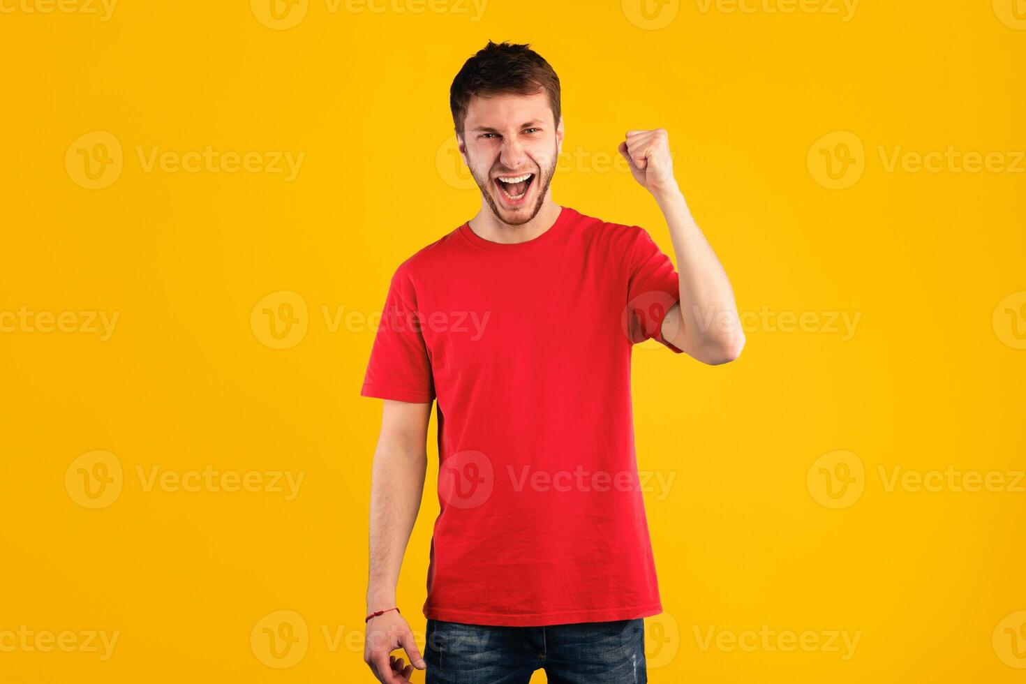 Celebrating Victory. Studio portrait of young man screaming hooray, shaking clenched fist raised up in the air, isolated over blue background. Excited guy cheering and yelling, supporting photo
