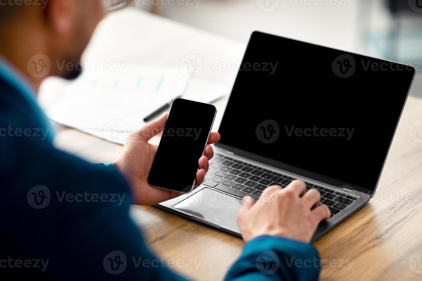 Cropped view of Arab businessman using laptop computer and smartphone with mockup for app or website design, closeup. Unrecognizable guy CEO working with modern gadgets, space for text photo