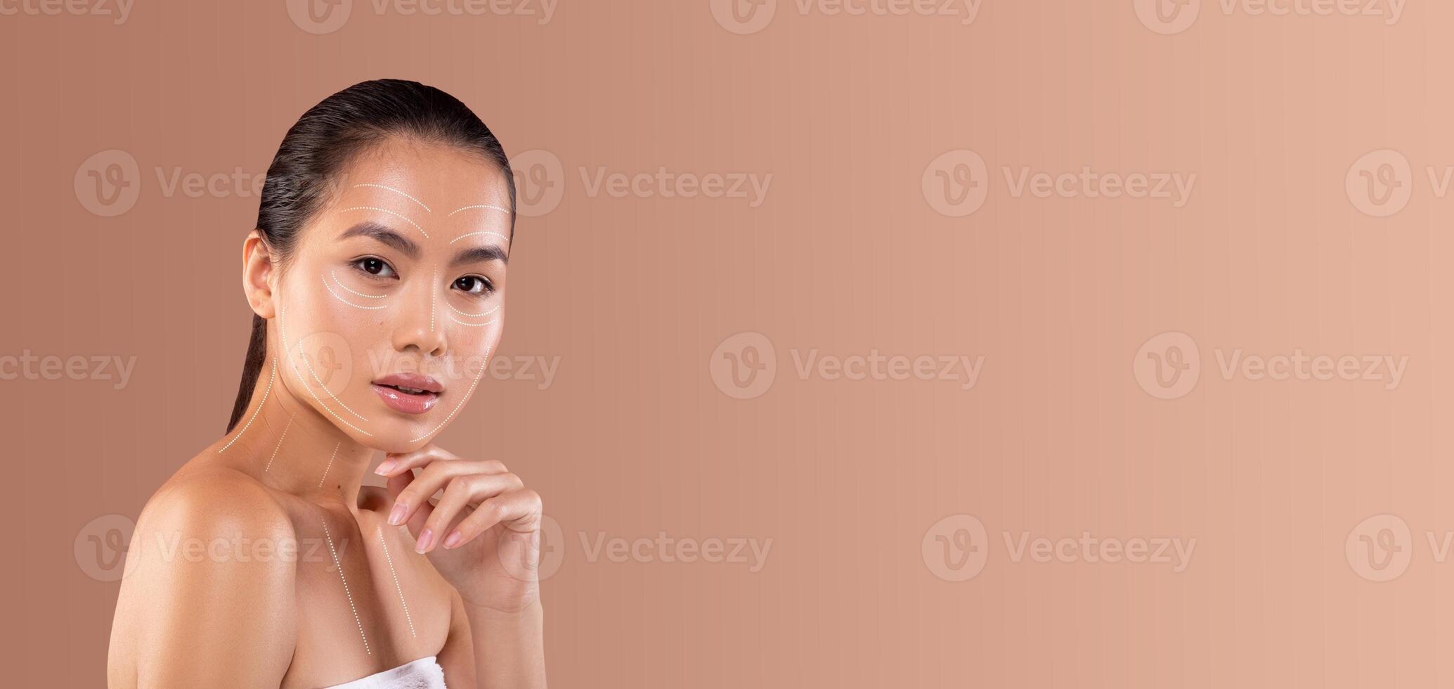 Asian woman applies a skincare product while relaxing and pampering herself in a minimalistic setting. The soft background enhances her natural beauty and care routine. photo